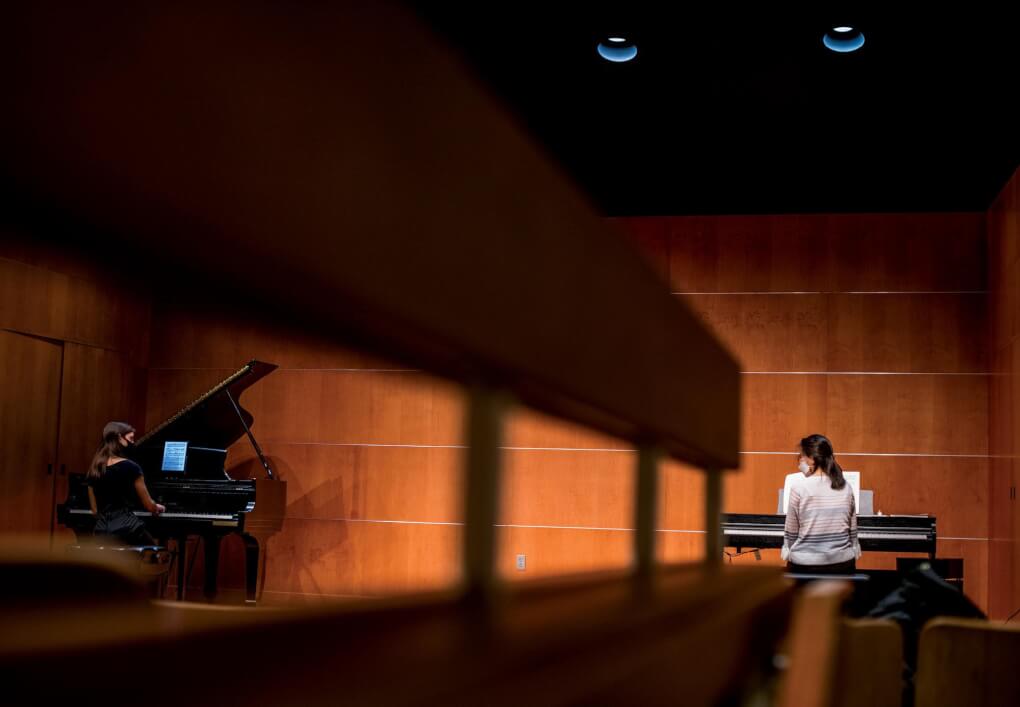 A student at a piano practices with her professor who is socially distanced at a keyboard